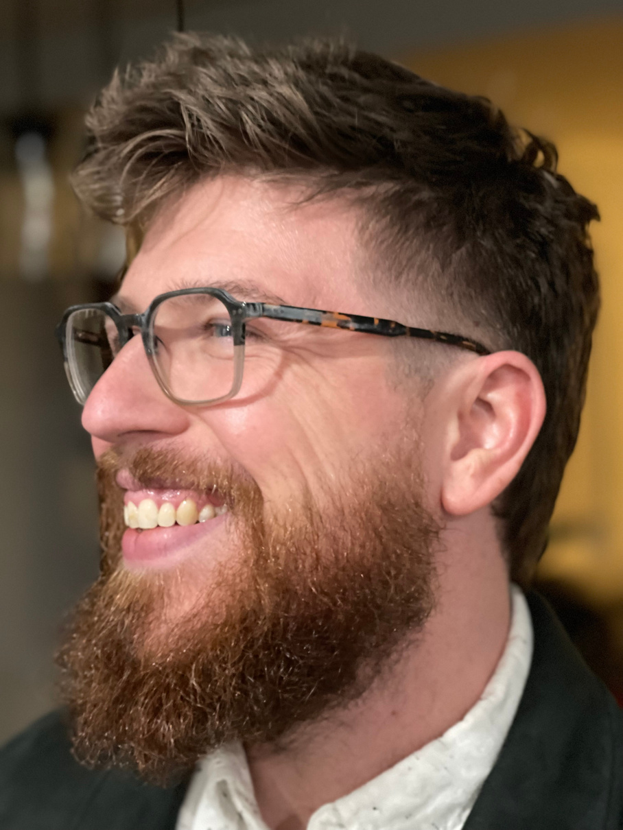 a good looking guy with a beard and glasses smiling after he had his hair cut into a perfect transitional mullet style perfect for the new season.