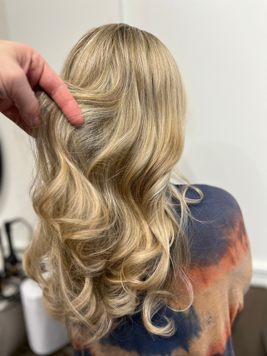 the back of a person's head with long blonde hair showing off fresh honey colored highlights. Her hair is very long and styled beautifully.