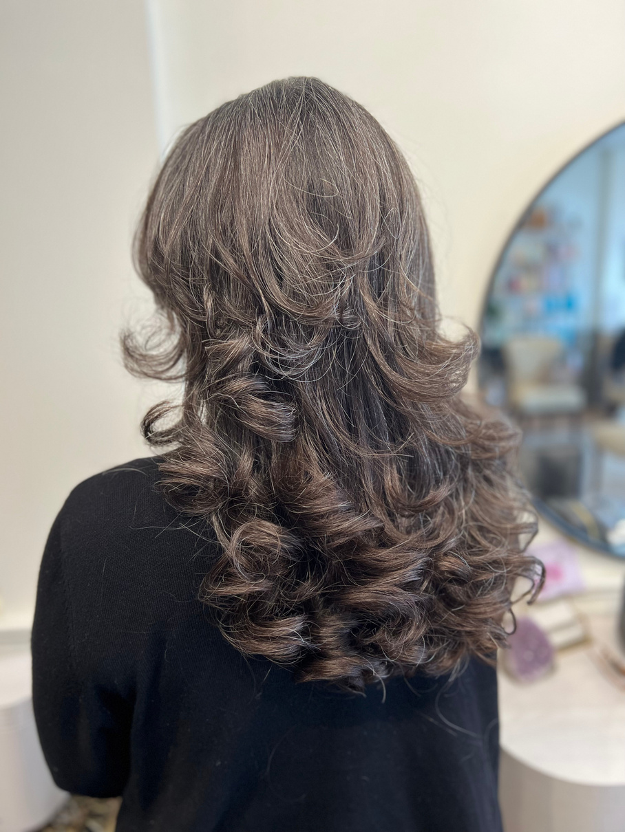 a person with long, wavy hair in front of a mirror posing for pictures after a fabulous blow-dry to highlight her glorious layers
